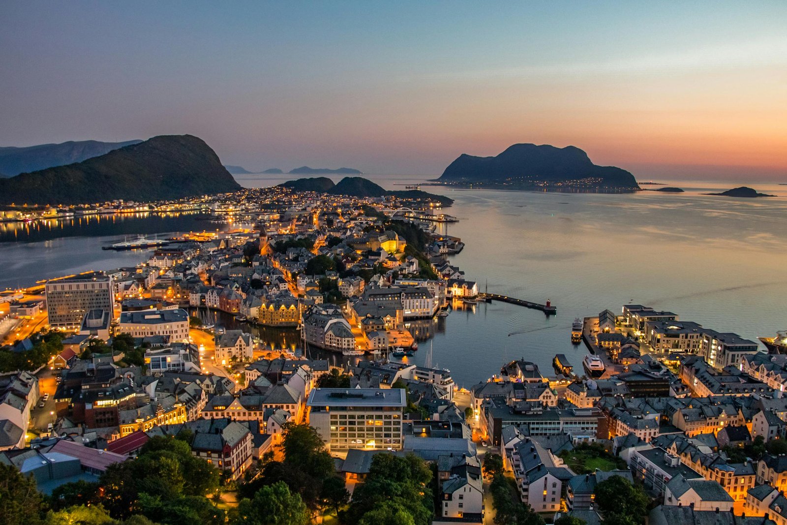 Explore the breathtaking skyline of Ă…lesund, Norway, illuminated against a stunning sunset over the harbor.